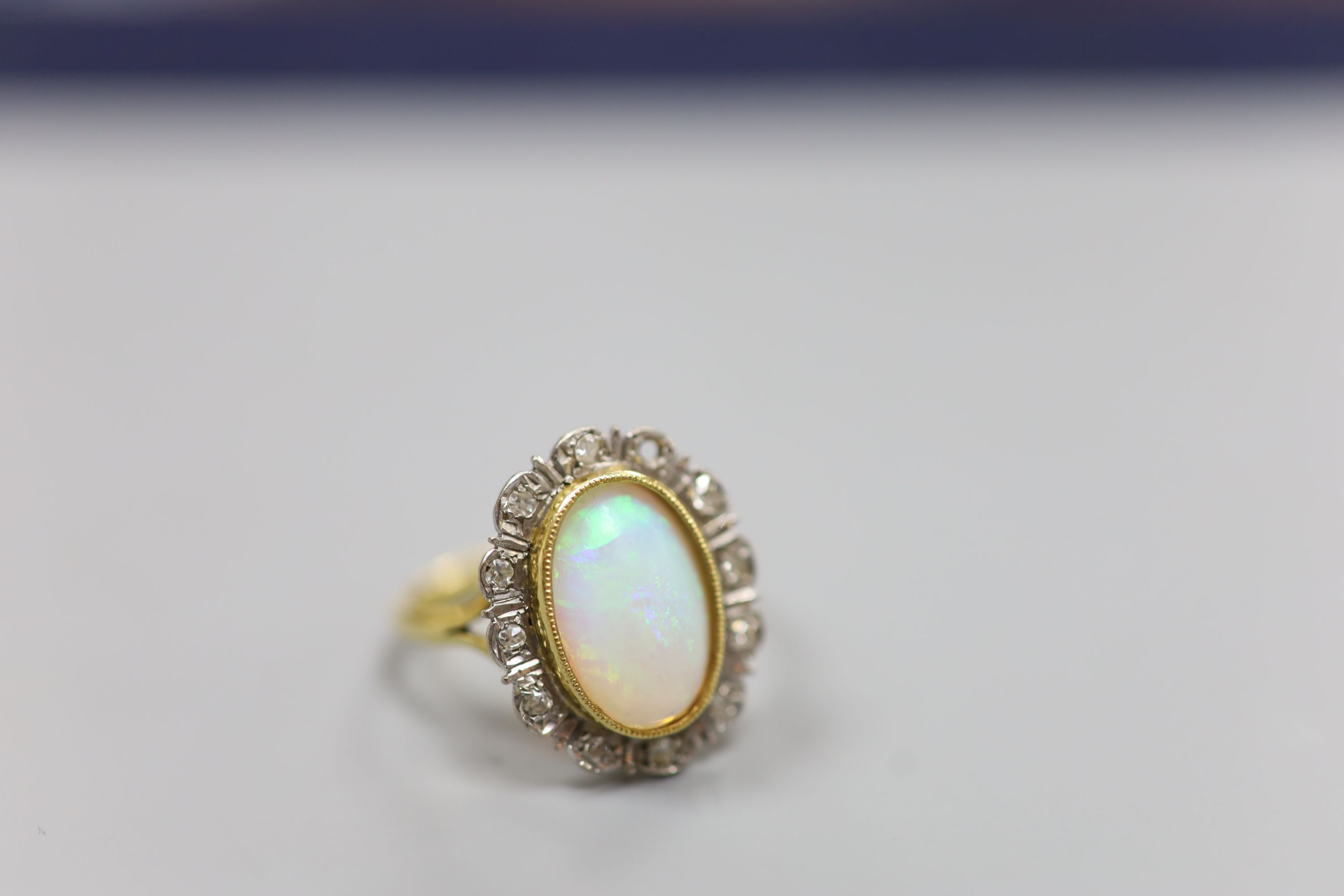 An 18ct, white opal and illusion set diamond oval cluster ring (one diamond missing)